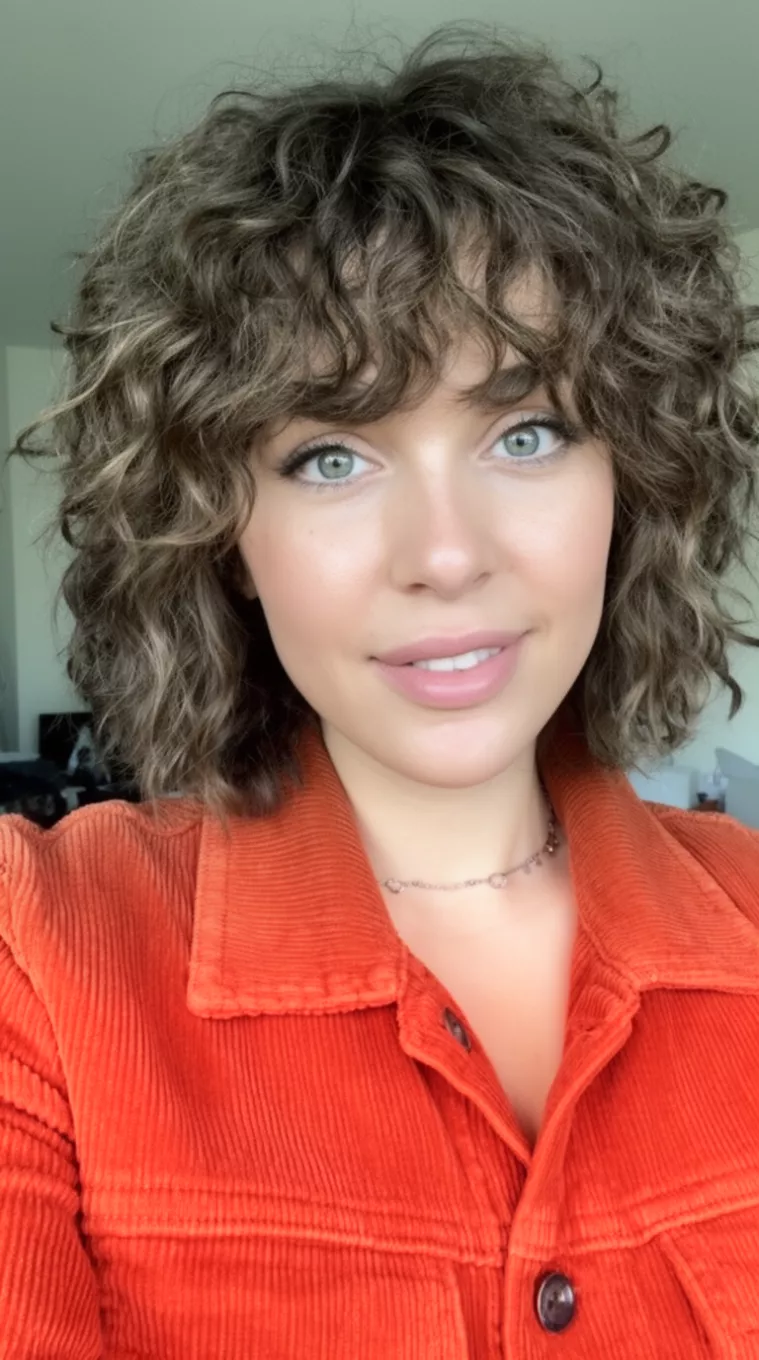 selfie of a 28-year-old woman wearing a rust orange corduroy jacket with a Curly layered shag cut