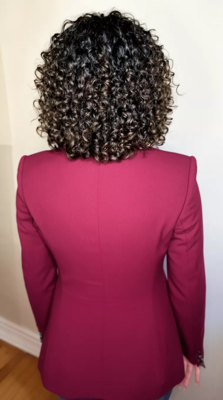 casual photo of a 31-year-old woman wearing a wine red blazer with a Curly bob with stacked layers at the back, back view