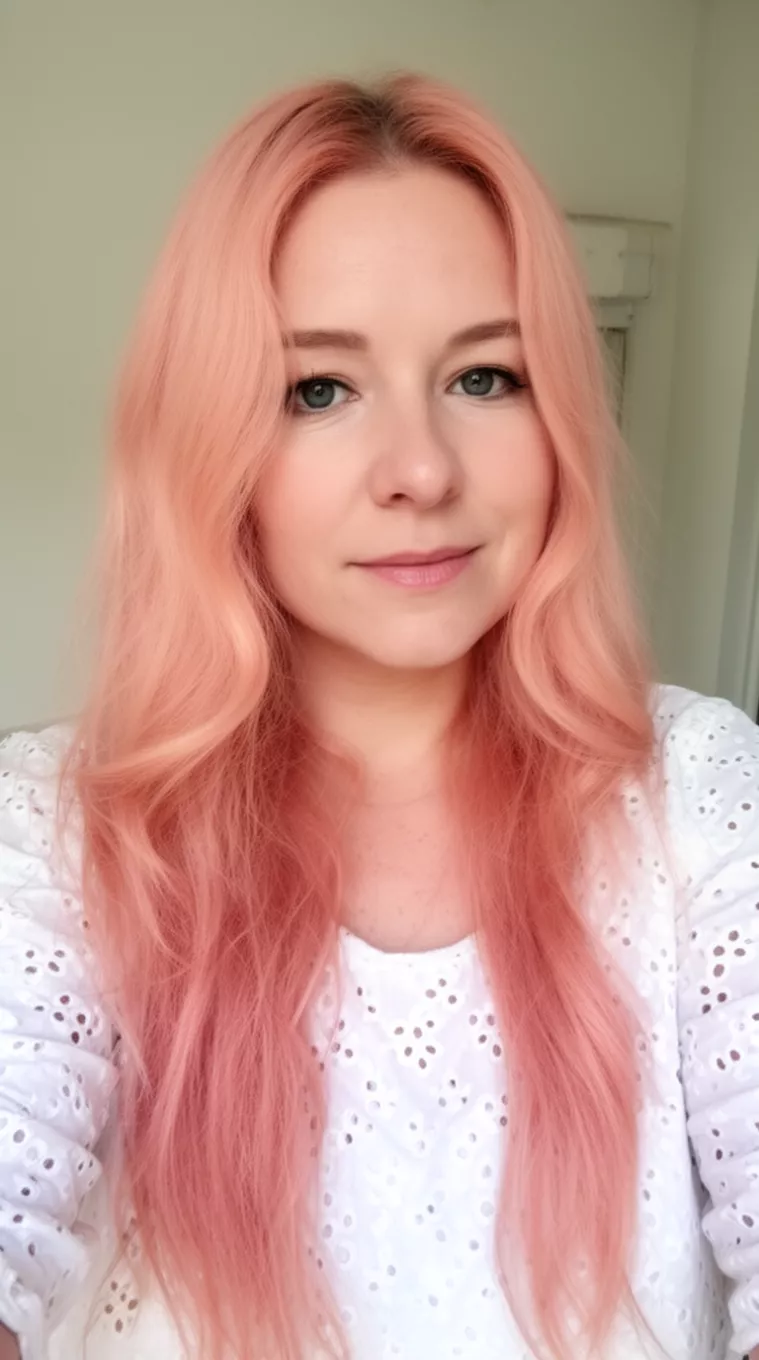 selfie of a 30-year-old woman wearing a white eyelet top with a Peach Glow colored long hairstyle, minimal background