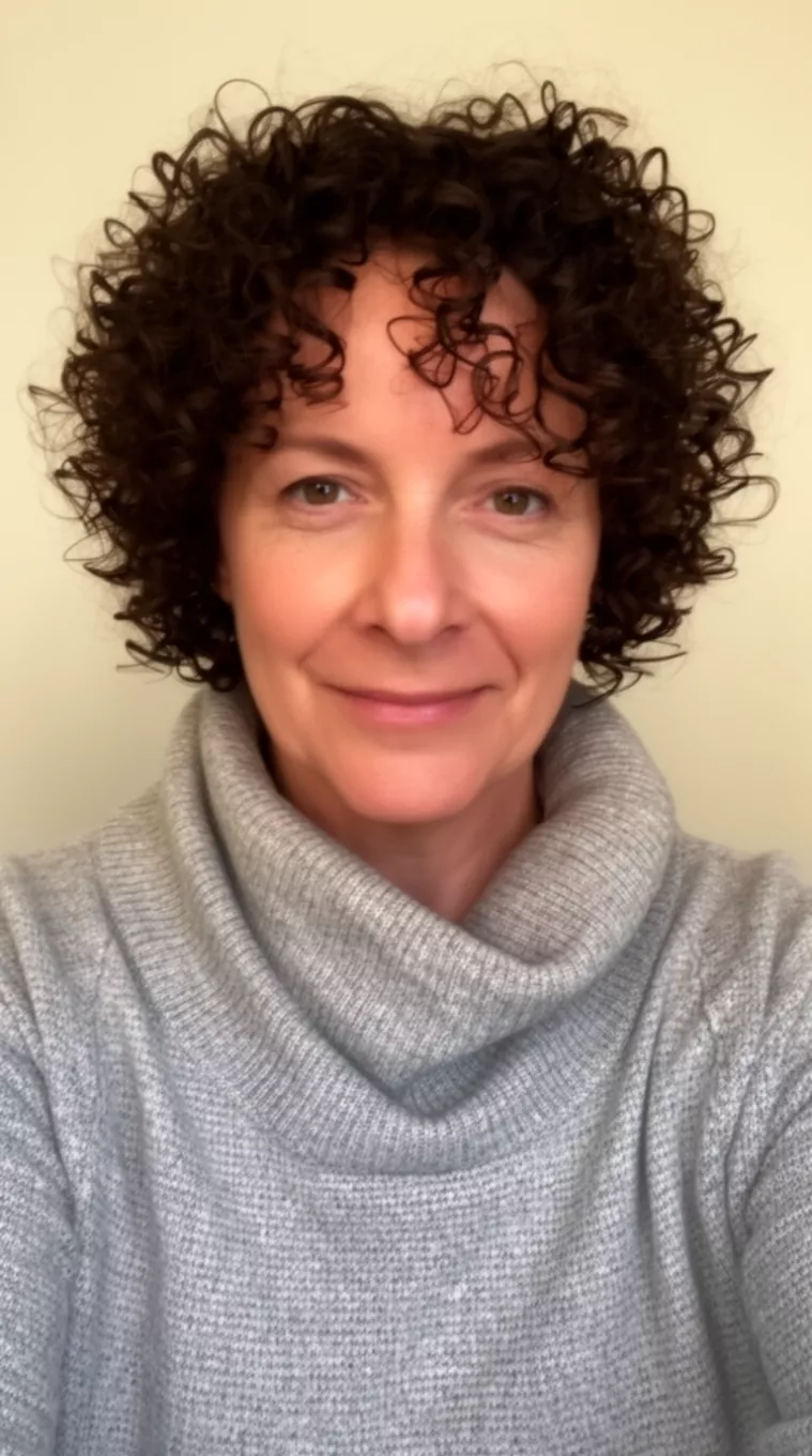 selfie of a 45-year-old woman wearing a cowl neck sweater with a Short Curly Ringlets hairstyle, minimal background