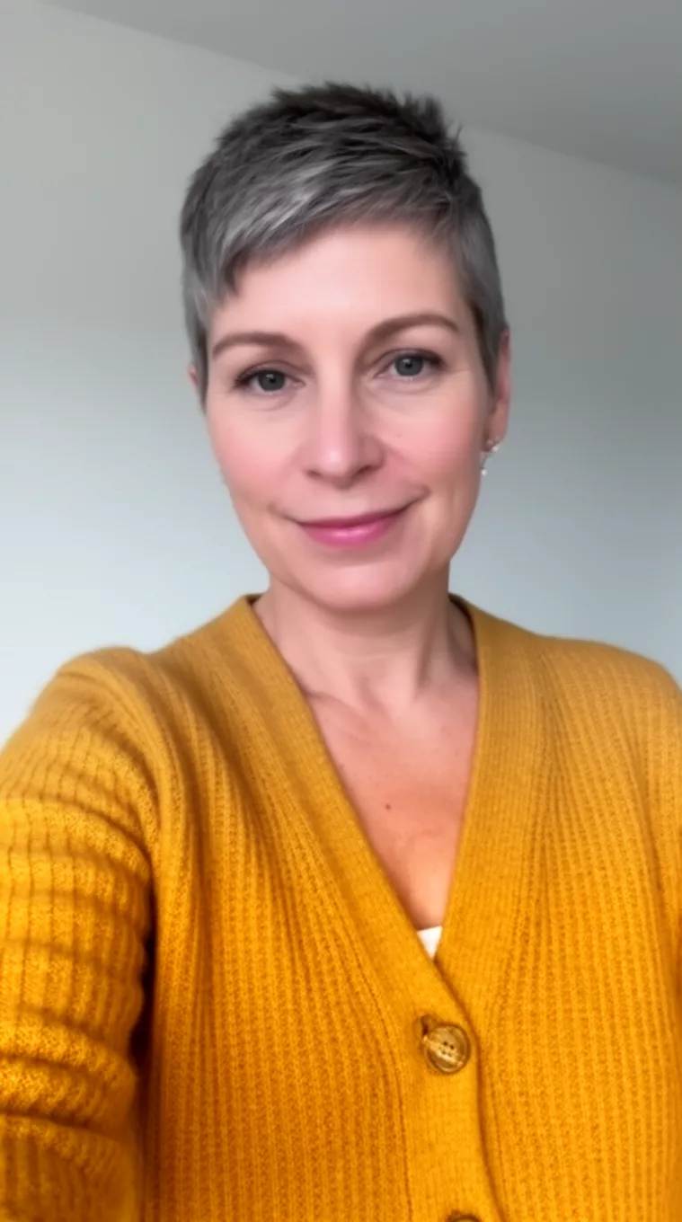 selfie of a 49-year-old woman wearing a mustard yellow cardigan with a Grown Out Crop hairstyle, minimal background