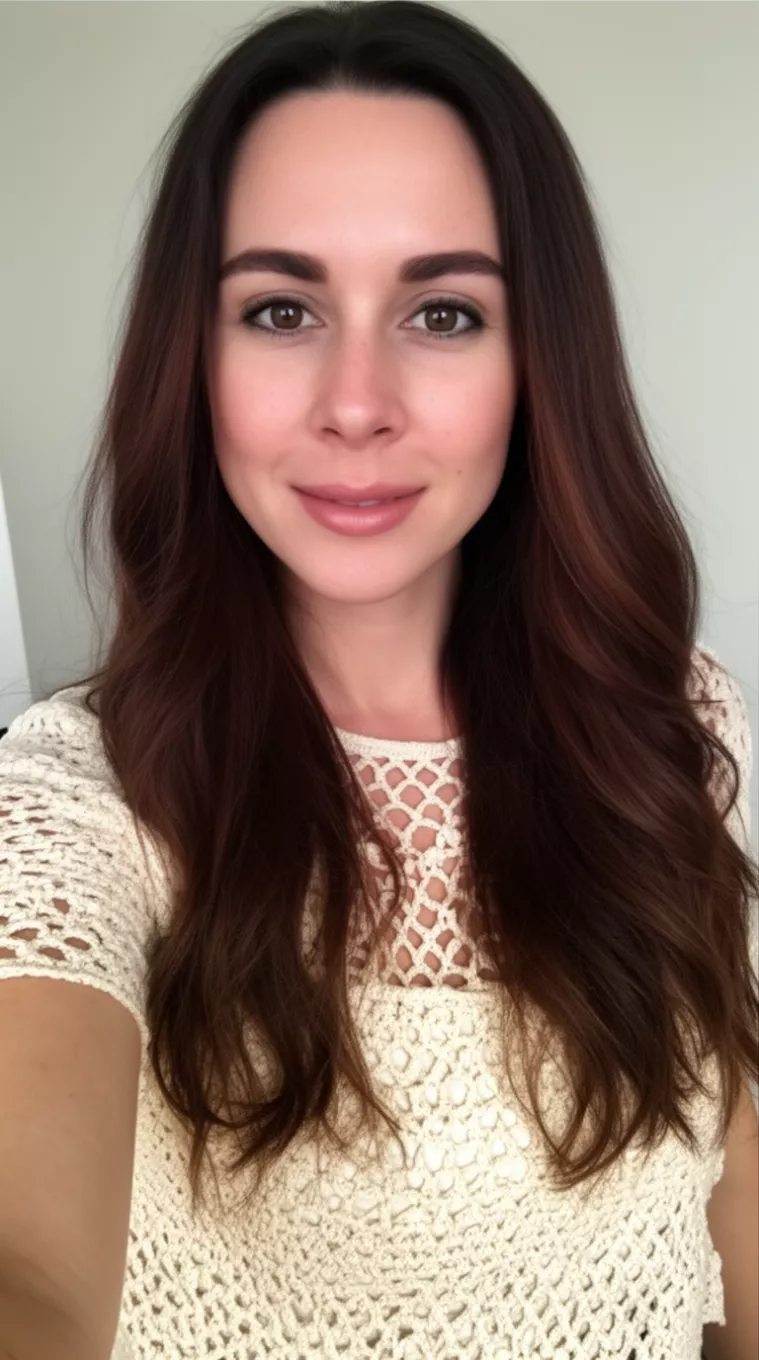 selfie of a 30-year-old woman wearing a cream crochet top with a Candlelit Brunette colored long hairstyle, minimal background