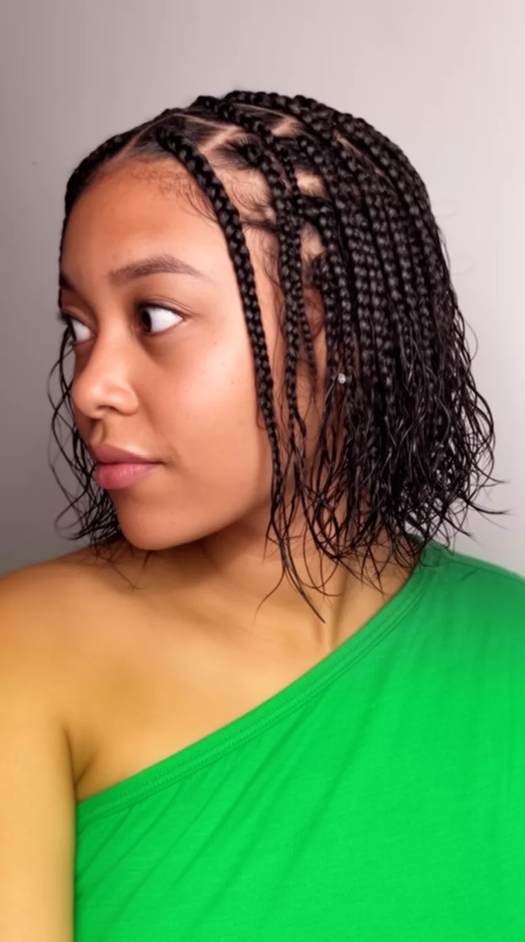 casual close-up photo of a 33-year-old woman wearing a green one-shoulder top with cornrow braids on top leading into a wet-look textured bob, side view, minimal background