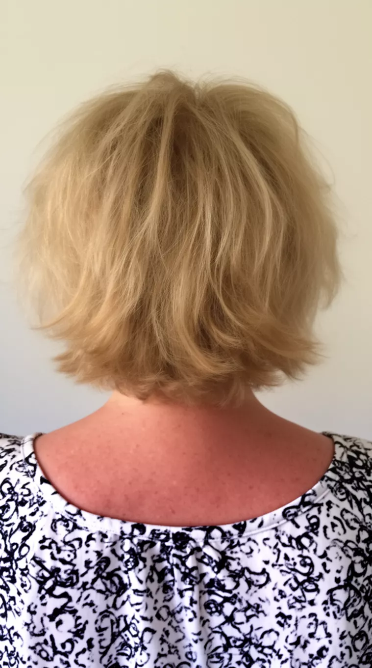 Messy Textured Blonde Bob casual close-up photo of a 62-year-old woman wearing a white and black patterned top with a messy, layered blonde bob hairstyle, back view, minimal background