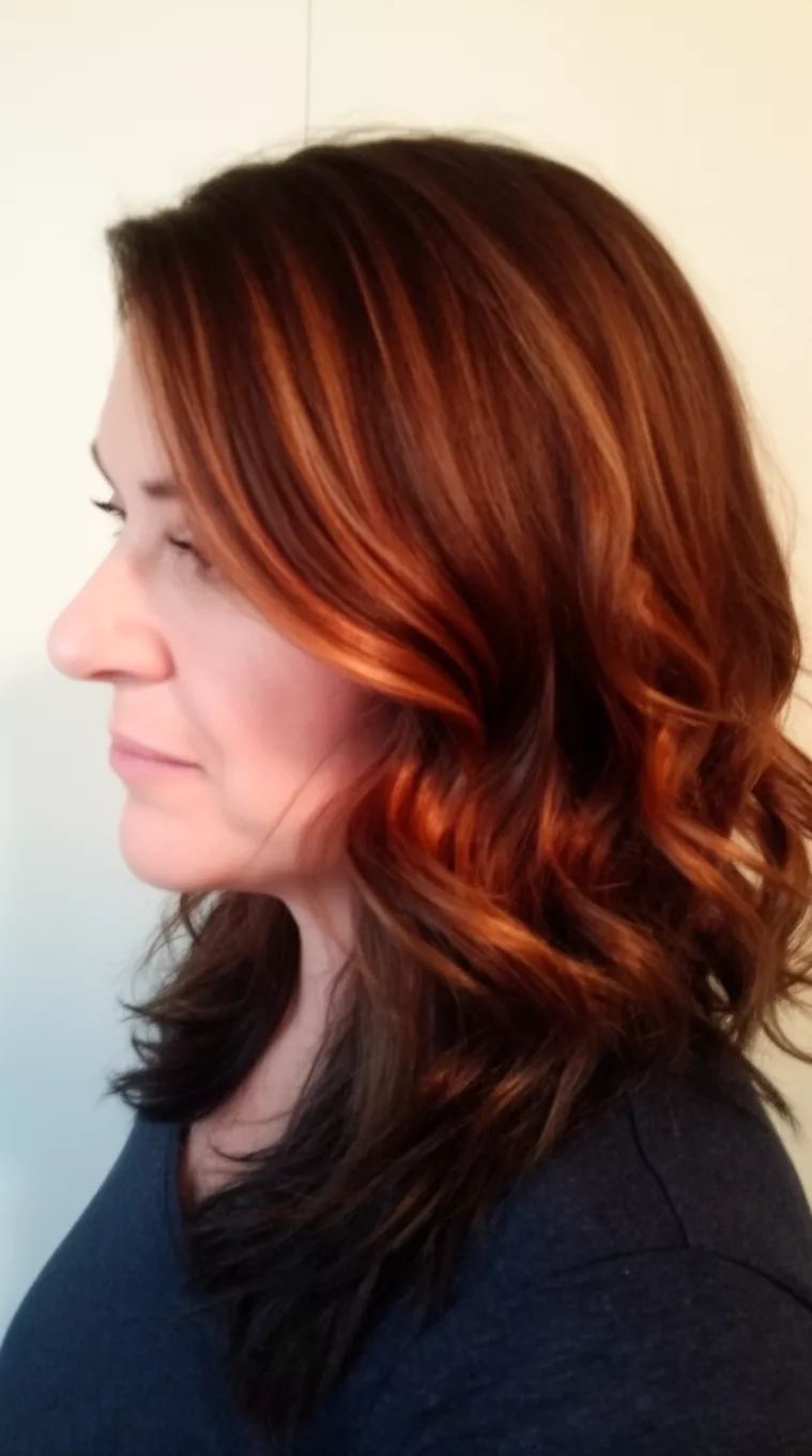 Copper Sun Tea casual photo of a 41-year-old woman wearing a dark top with a dark brown with coppery highlights colored medium length wavy hairstyle, side view, minimal background.