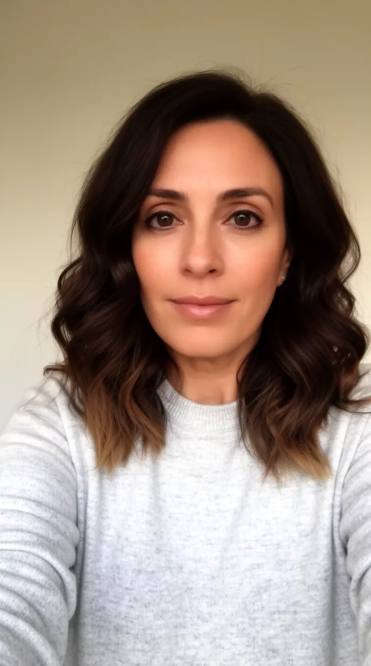 selfie of a 38-year-old woman wearing a light grey sweater with a Subtle Coffee To Toffee Ombre colored medium-length wavy dark brown hair with subtle ombre hairstyle, front view, minimal background.