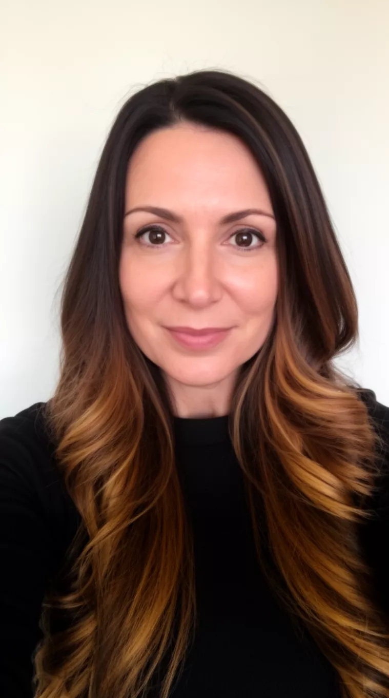 selfie of a 39-year-old woman wearing a black top with a Caramel Ribbon Brunette colored long dark brown hair with warm caramel highlights hairstyle, front view, minimal background.
