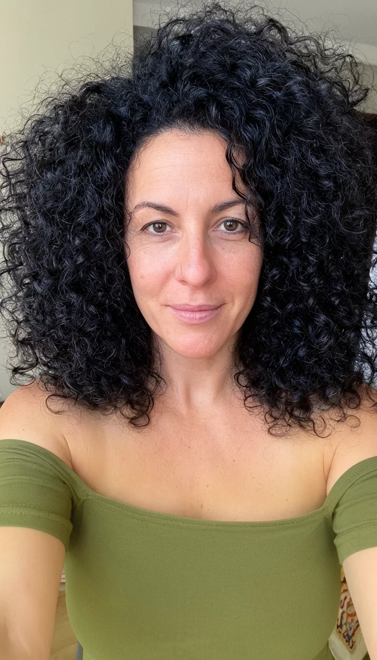 selfie of a 36-year-old woman wearing an off-the-shoulder olive green top with a large, voluminous mane of dark, tightly curled hair, front view, close-up shot
