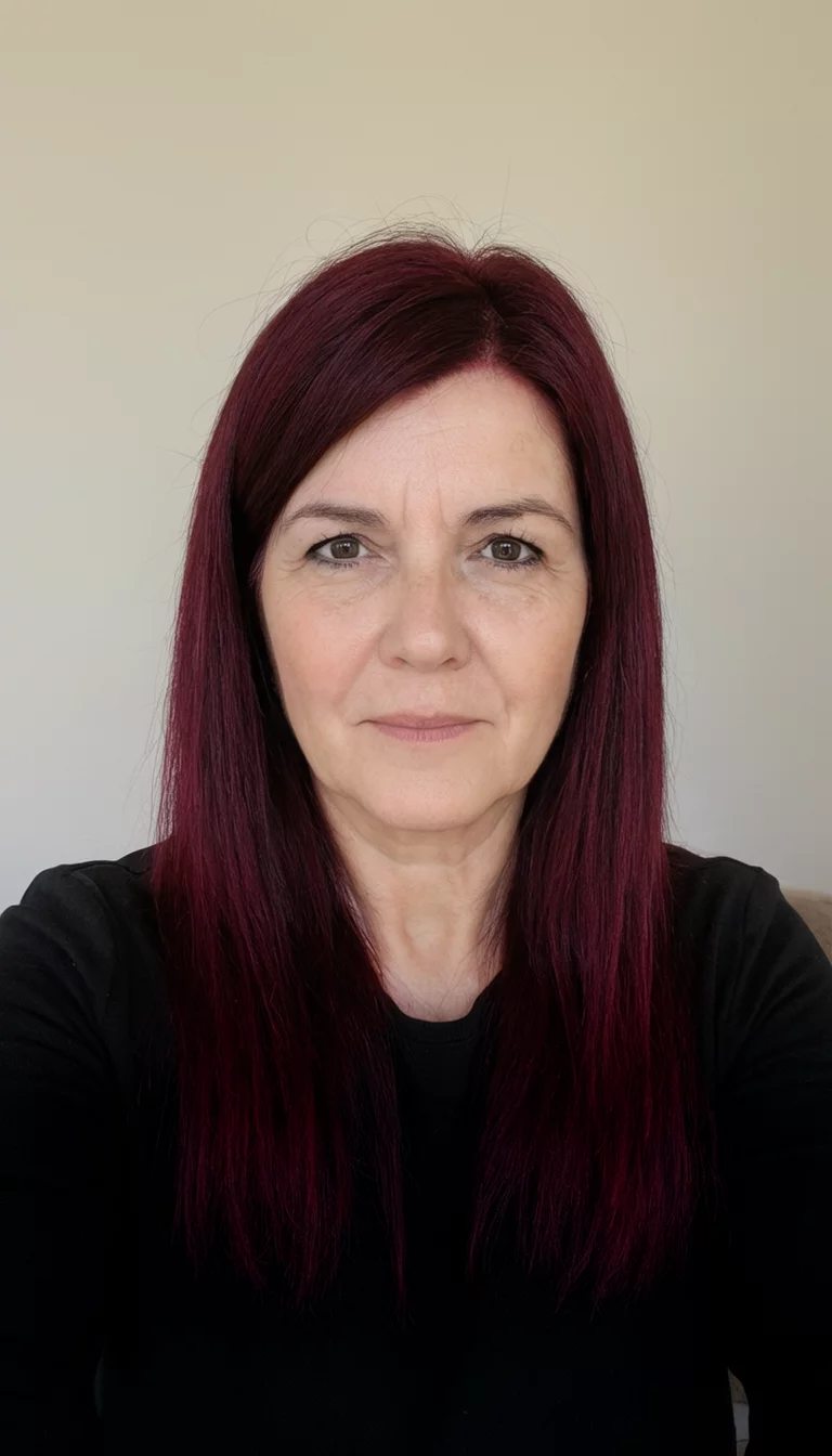 selfie of a 43-year-old woman wearing a black top with a dark red hair colored straight hairstyle, front view, simple background