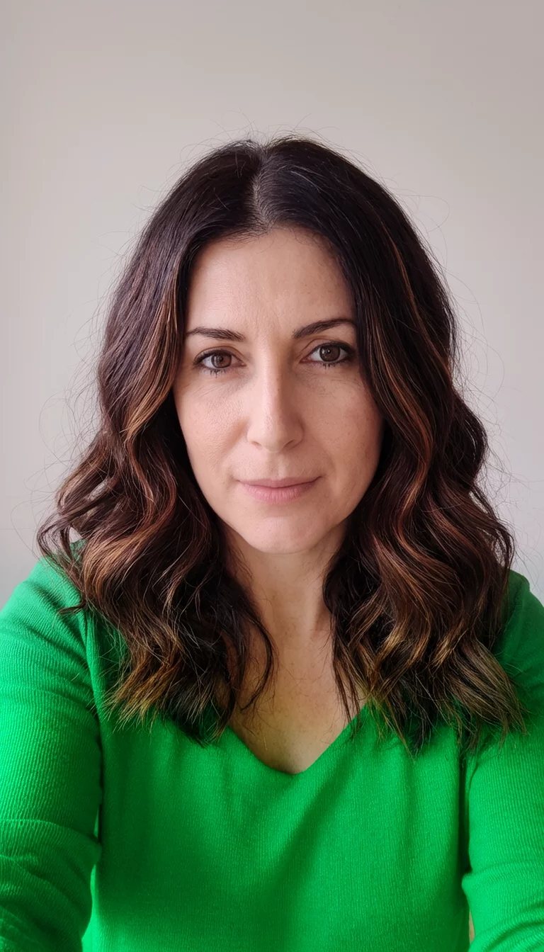 selfie of a 33-year-old woman wearing a green top with a dark brown hair with subtle brown highlights colored wavy hairstyle, front view, neutral background