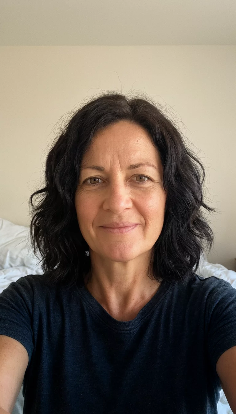 selfie of a 41-year-old woman wearing a dark shirt with dark shoulder-length wavy hair hairstyle, front view, simple bedroom background