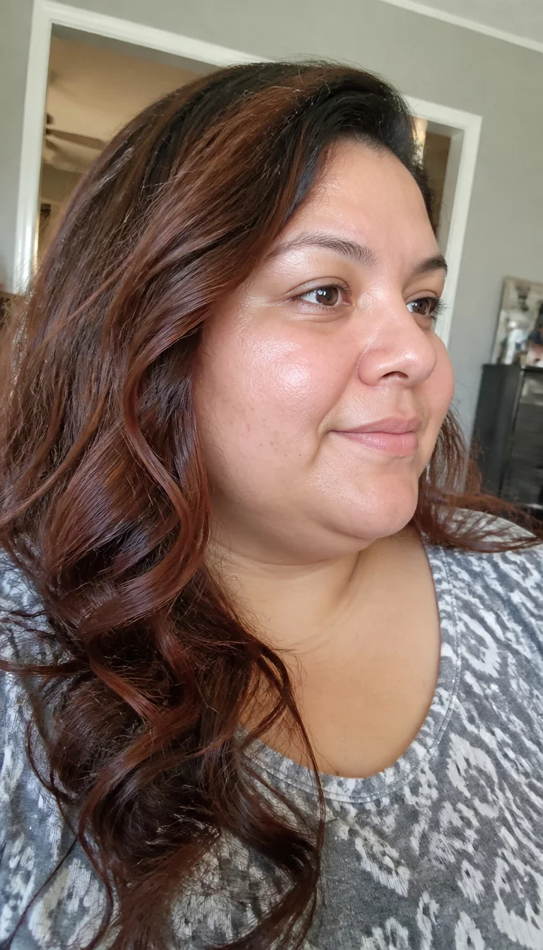 casual photo of a 33-year-old plus size Latina woman with a chubby face and a soft, wide nose. Her face skin has a dewy, natural texture. The eyes are dark brown. She is wearing a grey and white patterned top with long, wavy, dark brown hair with subtle auburn highlights hairstyle, side view, indoor residential background.