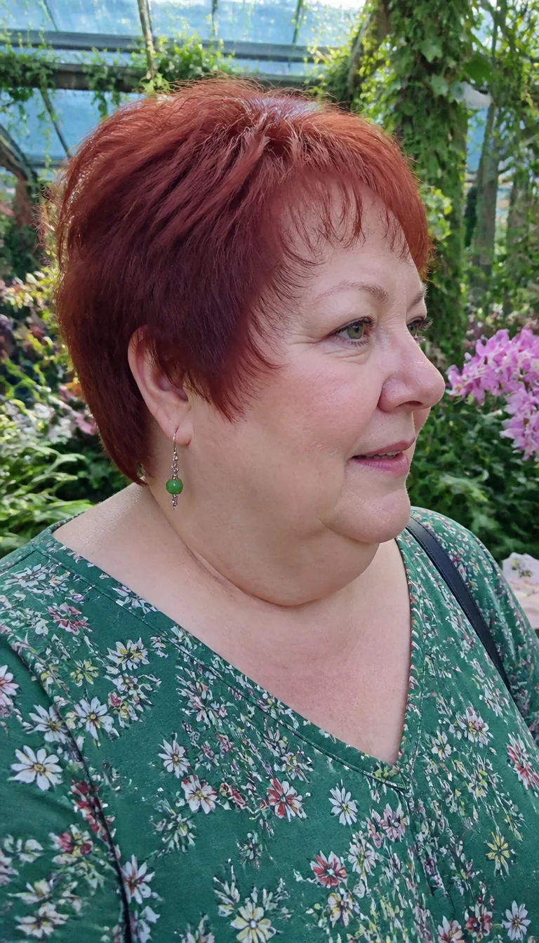 Choppy Red Hair In Profile casual photo of a 65-year-old plus size Caucasian woman with a chubby face and pointed nose. Her face skin has fair texture. The eyes are green. She is wearing a green floral top with a short choppy red hair hairstyle, side view, botanical garden background.