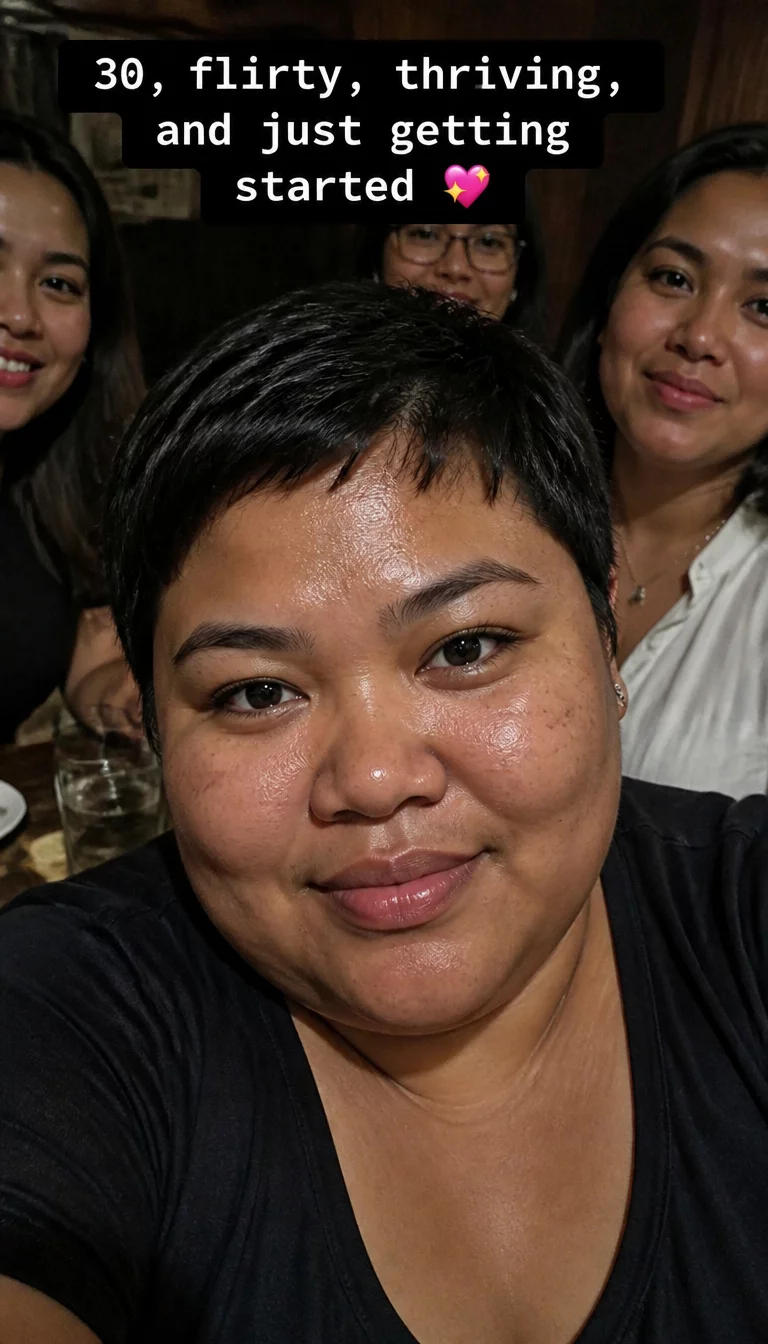 selfie of a 30-year-old plus size woman with a chubby face and a soft, wide nose. The skin is heavily textured with a complex pattern of beauty marks and a slightly oily T-zone. The eyes are dark. She is wearing a casual top with a stylish pixie hairstyle, front view, group setting with text overlay.
