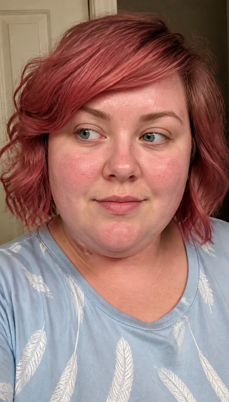 Messy Pink-Red Wavy Bob selfie of a 27-year-old plus size fair complexion woman with a chubby face and a slightly flared nose. The skin is heavily textured with a complex pattern of pink undertones and a small scar on the jawline. The eyes are gray. She is wearing a light blue top with white feather patterns with a reddish-pink, messy wavy bob with side fringe hairstyle, front view looking slightly aside.