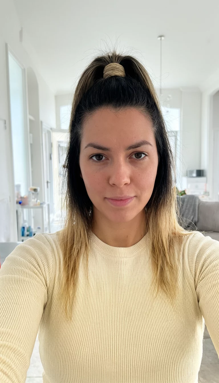 selfie of a 27-year-old woman wearing a cream-colored ribbed top with a very high ponytail featuring dark hair with blonde highlights, front view, bright indoor background
